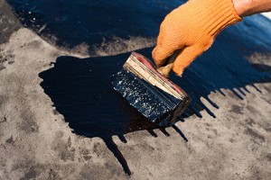 Roofer cover the concrete base, polymer modified bitumen waterproofing primer. A worker brushes cover concrete, bitumen-rubber primer.